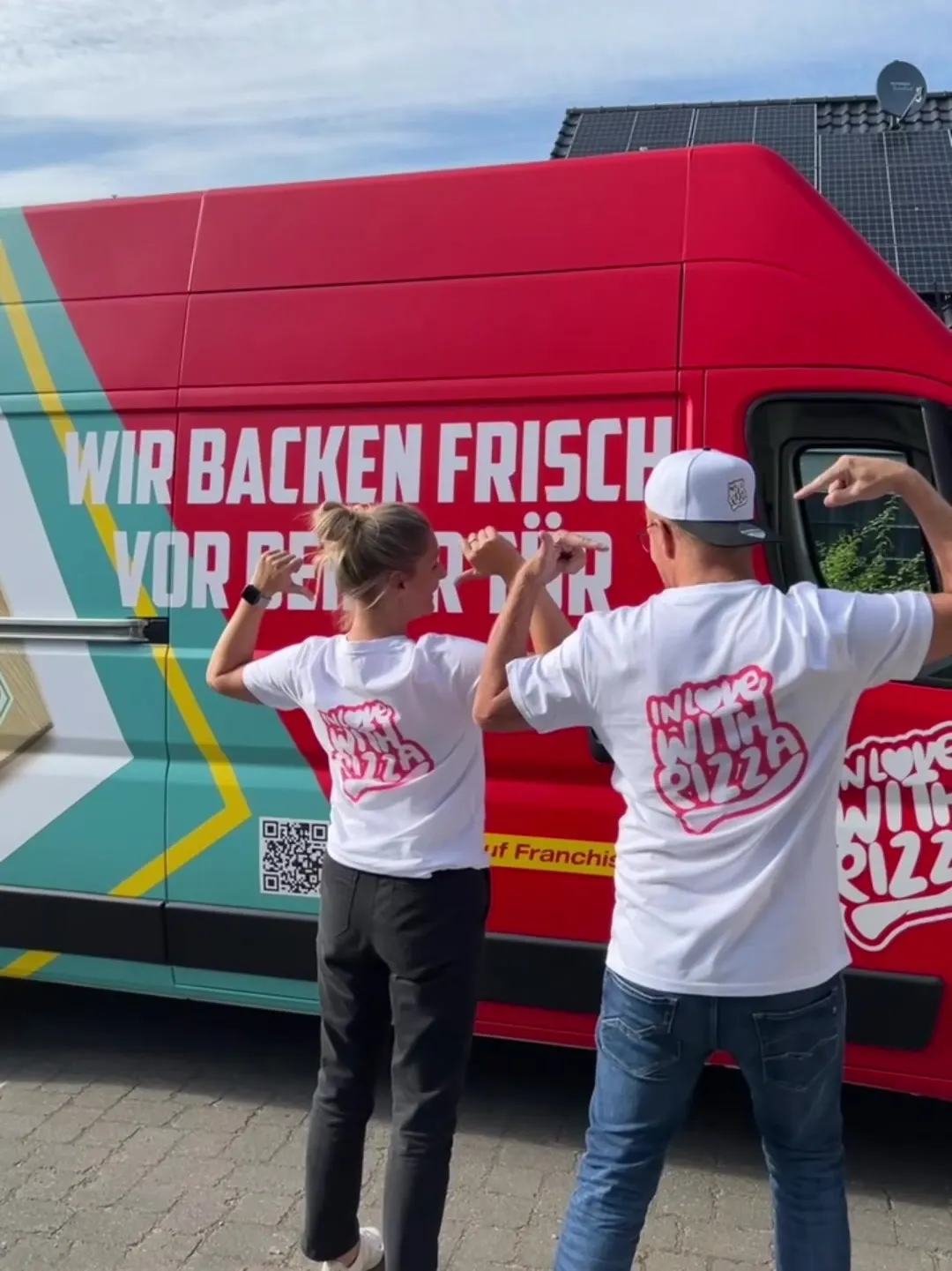 Zwei Personen in In-love-with-Pizza-Shirts zeigen auf den roten Pizza-Van