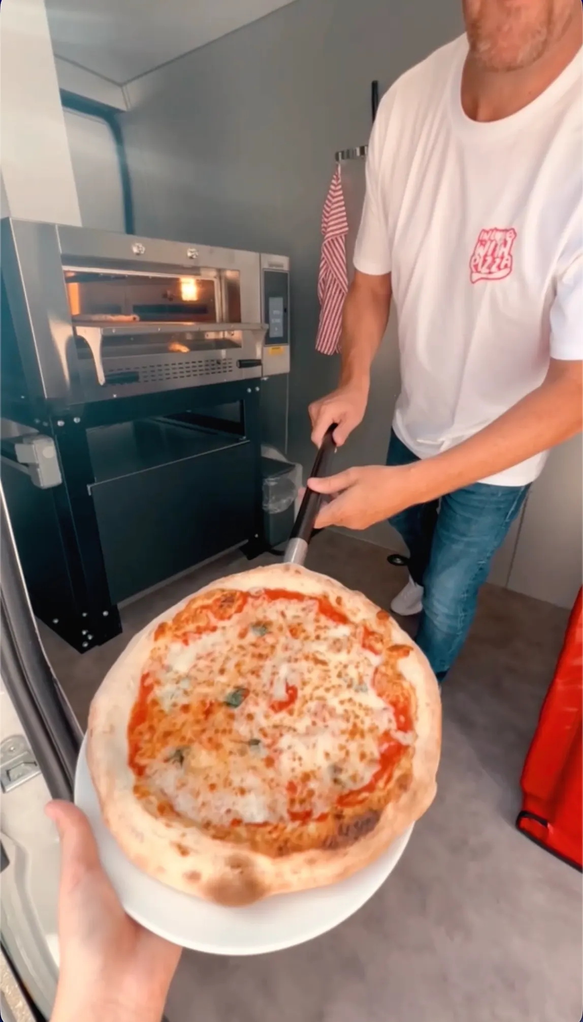 Unser Pizzabäcker holt eine fertige Pizza aus dem Ofen im Pizza-Van